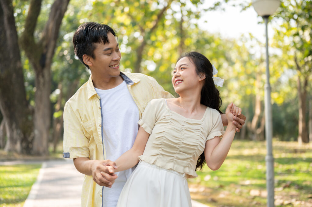 A lovely young Asian couple is dancing in a beautiful green park together. flirting, dating, honeymoon, boyfriend and girlfriend, relationship