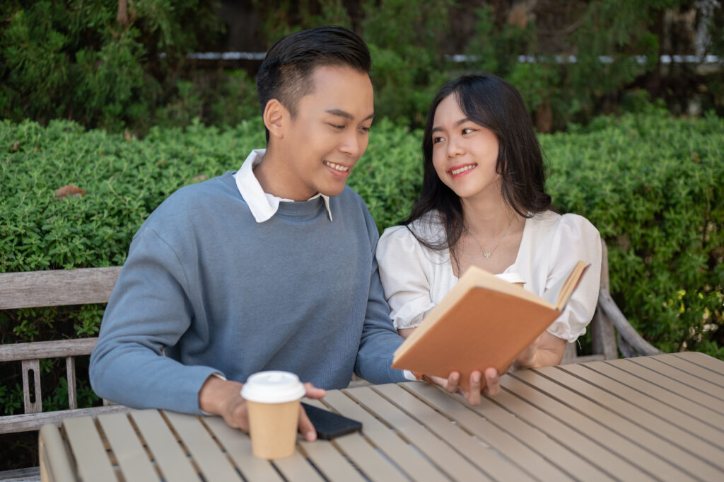 Young adorable Asian couple spending time together in the park, sitting close to each other. hanging out