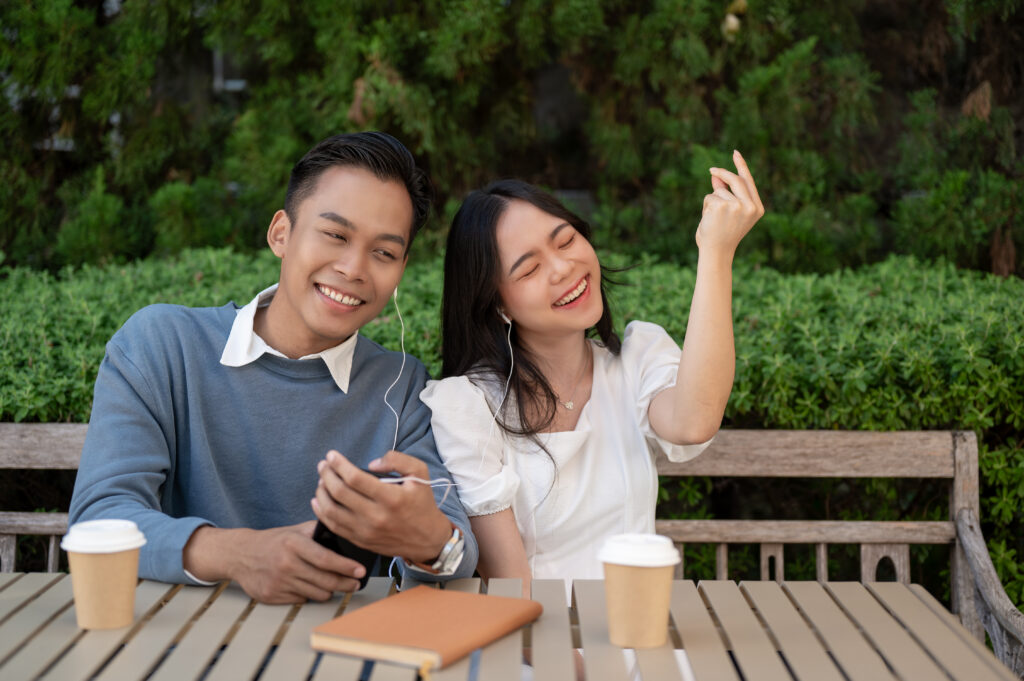 Young Asian couple listening to music together, having fun together in the green park. Couple concept.